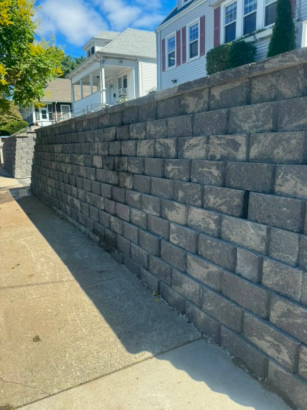 Charcoal segmental block retaining wall along a graded backyard in a Massachusetts neighborhood